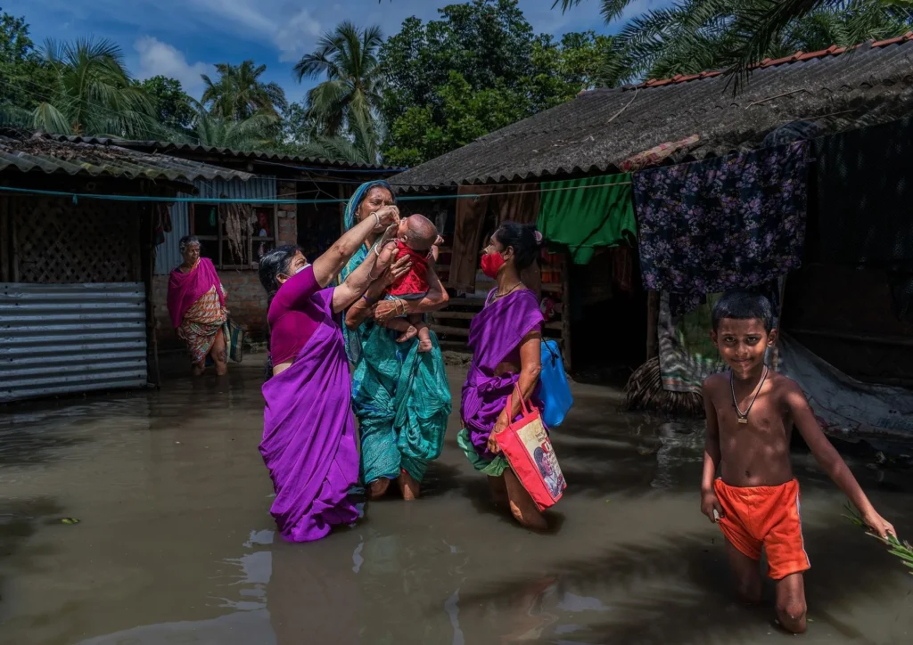 Women and children wading through floodwater in a village